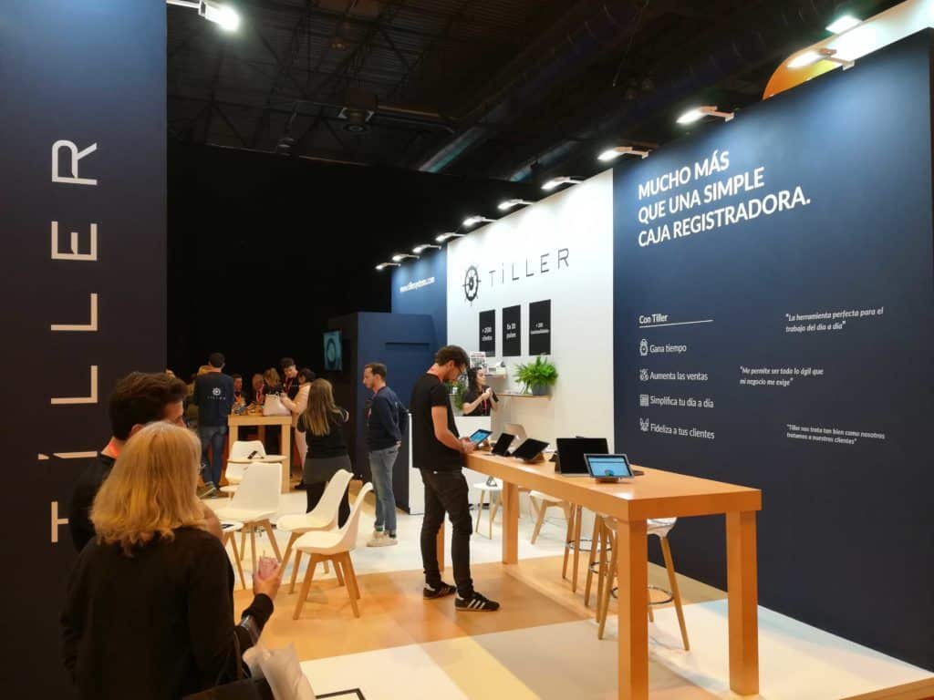 Stand de Tiller con mostradores para terminales, pantallas y mesas de reunión