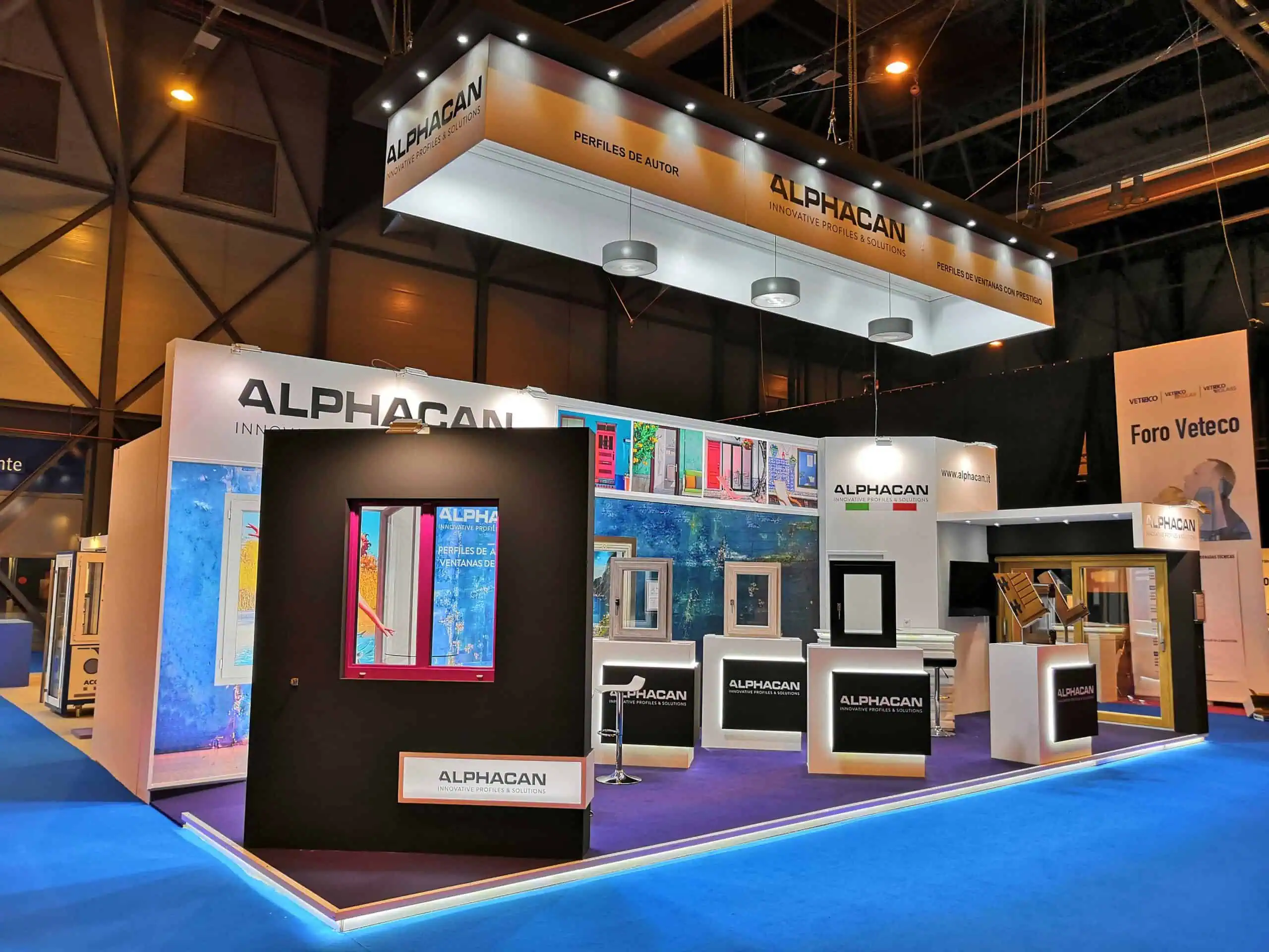 ALPHACAN stand with illuminated window profile galleries and suspended banner at Veteco IFEMA Madrid at night