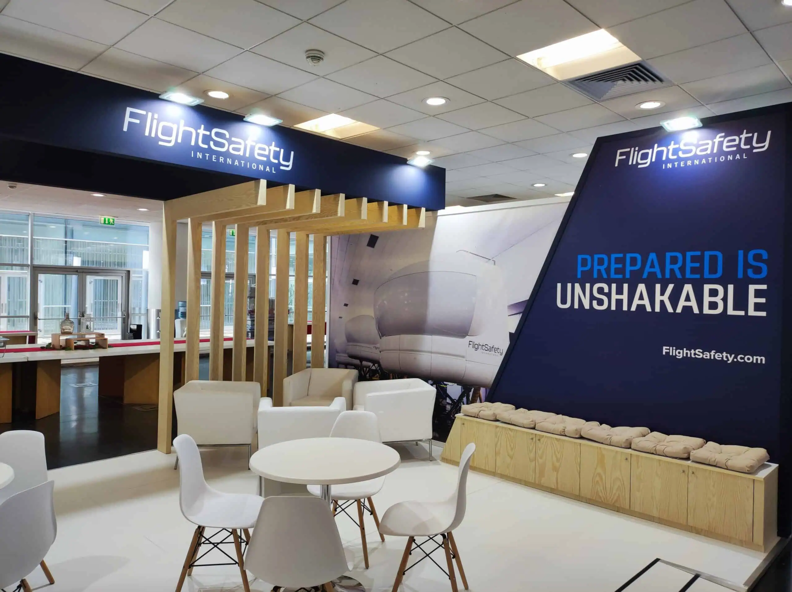 FlightSafety International tradeshow booth with navy branding wooden slats and lounge seating at European venue
